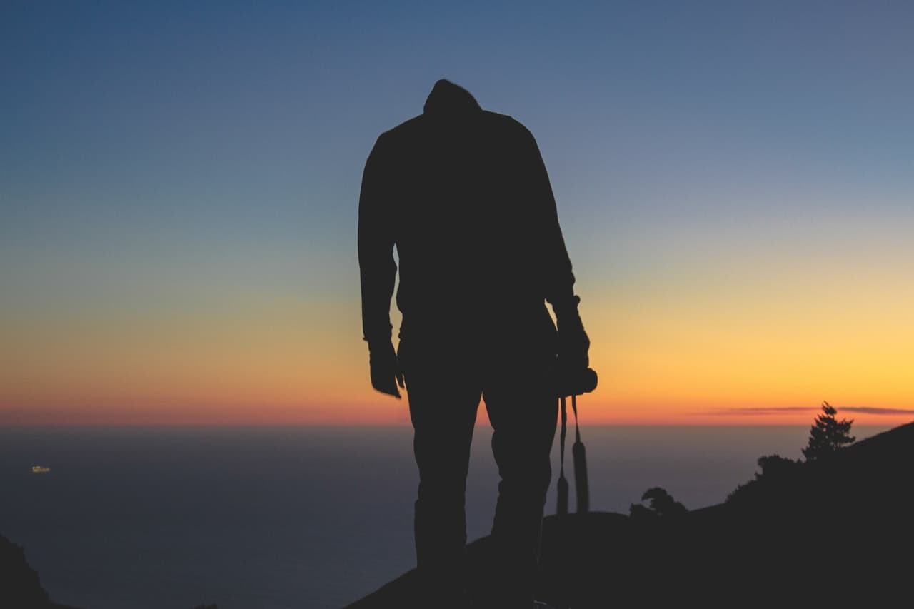 A photographer silhouetted against a sunset, camera in hand